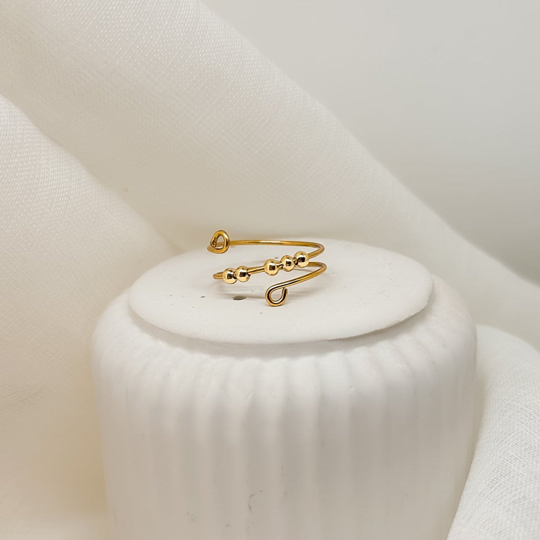 Filigraner, handgemachter Goldring im minimalistischen Design, Nahaufnahme auf beigem Schmuckpodest, hochwertiges Produktfoto für Damen-Schmuck.