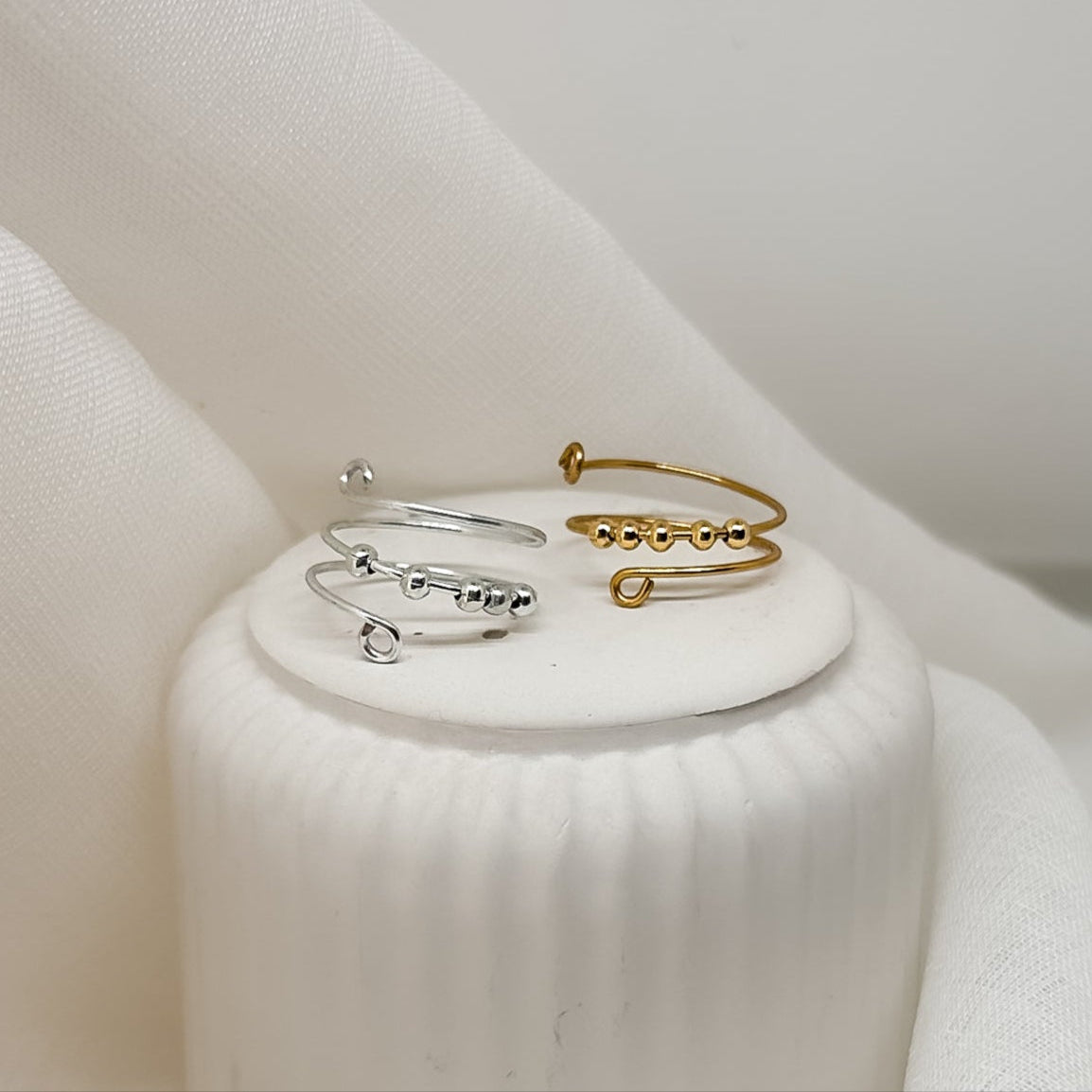 Minimalistische Damenringe, ein Goldring und ein Silberring, handgefertigt, stilvoll nebeneinander auf hellem Schmuckpodest präsentiert, hochwertiges Produktfoto.