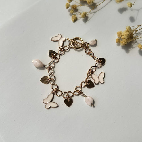 Flach liegendes Goldarmband mit weißen Schmetterlingen und Herzen, dekoriert mit Trockenblumen – romantischer Schmuckstil.