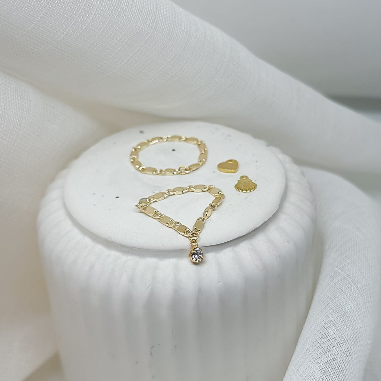 goldene Ringe und Charms auf Podest mit weißem Stoff – minimalistischer Schmuck