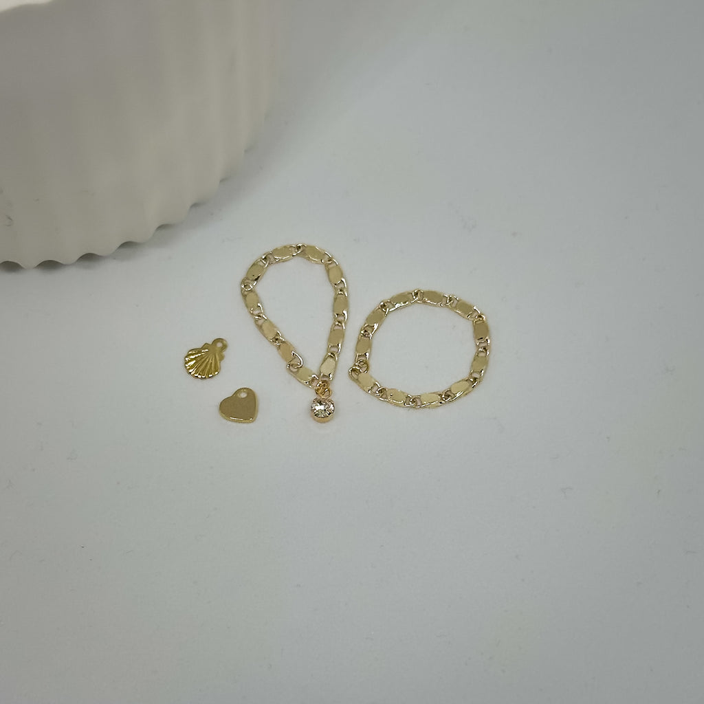 goldene Ringe mit Herz- und Muschel-Charm flach auf weißem Hintergrund
