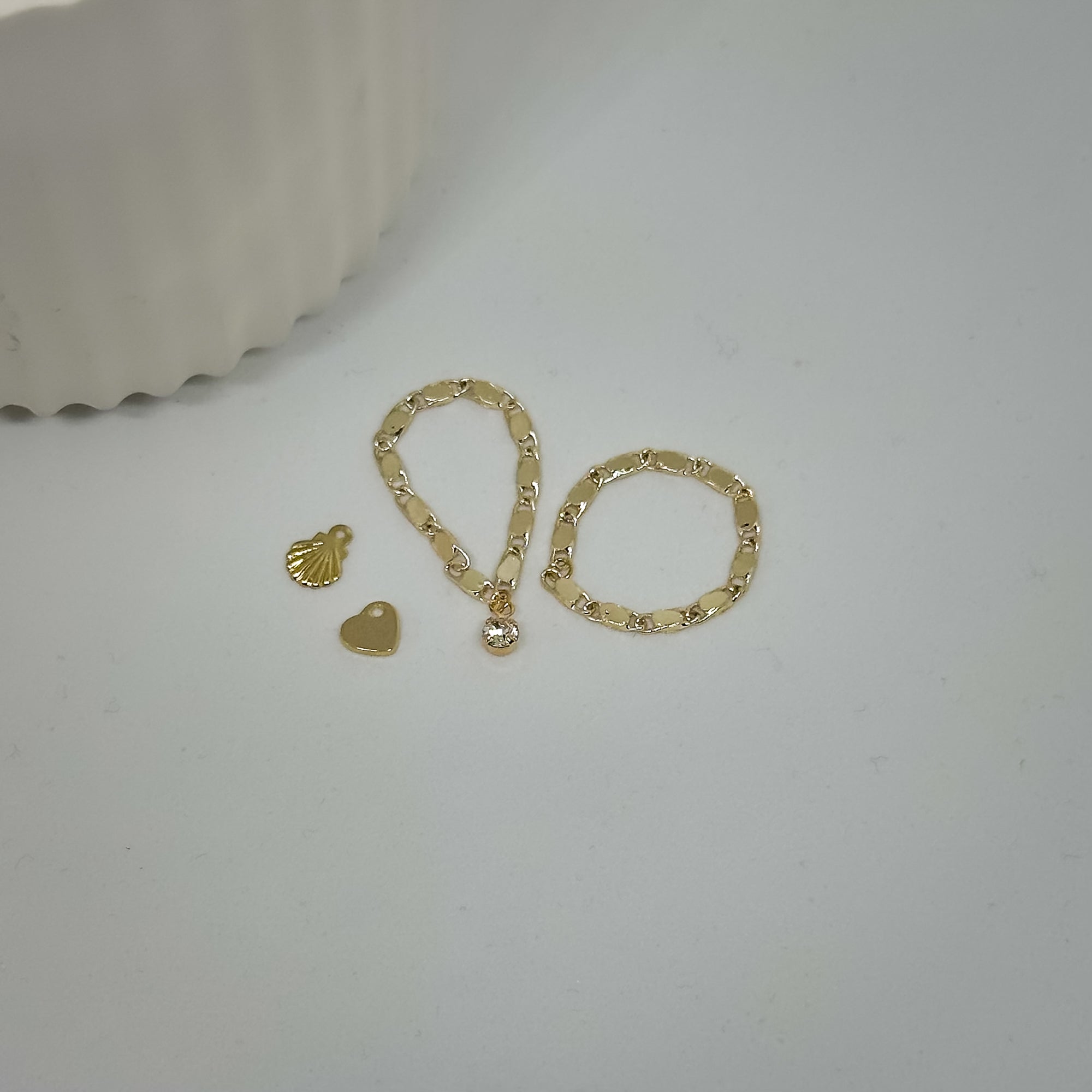 goldene Ringe mit Herz- und Muschel-Charm flach auf weißem Hintergrund