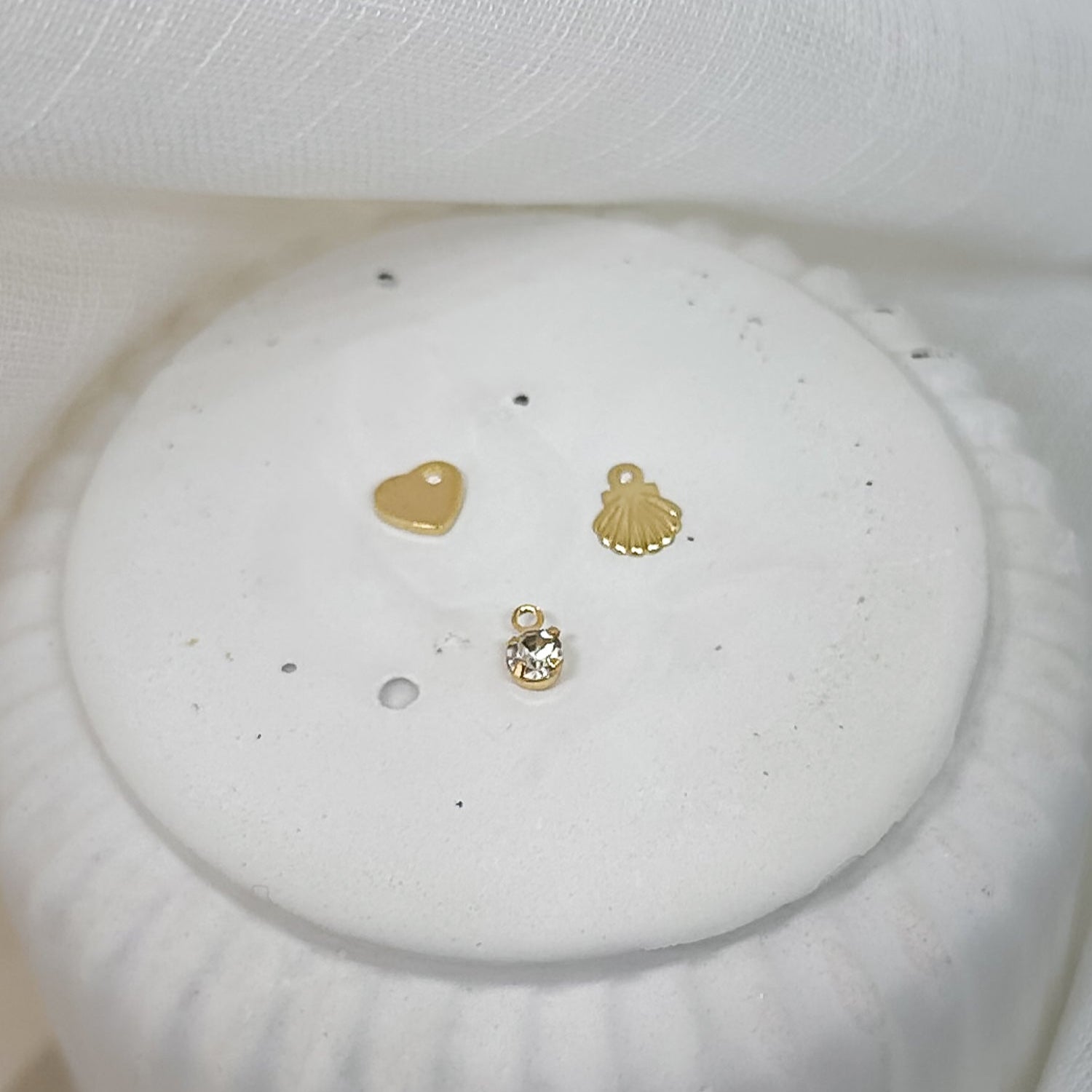 goldene Charm-Anhänger Herz Muschel Kristall auf weißem Podest – filigraner Schmuck