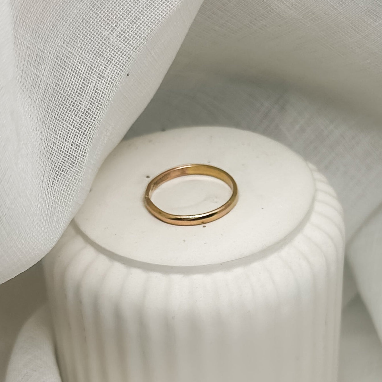 Goldfarbener Ring auf weißer Dose mit Drapierung – Schmuckfoto
