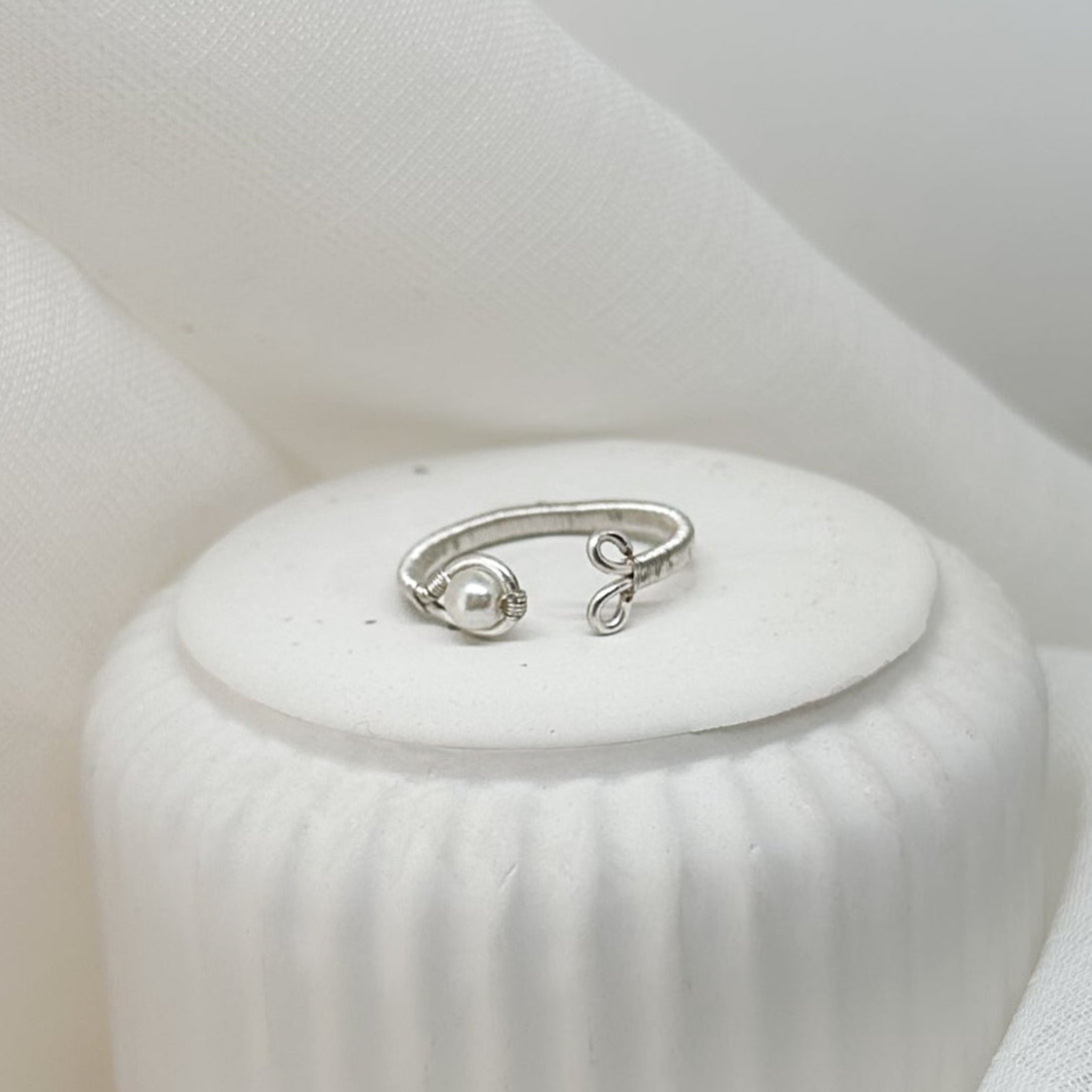 Offener Silberring mit Perle auf weißem Podest – minimalistisch und elegant