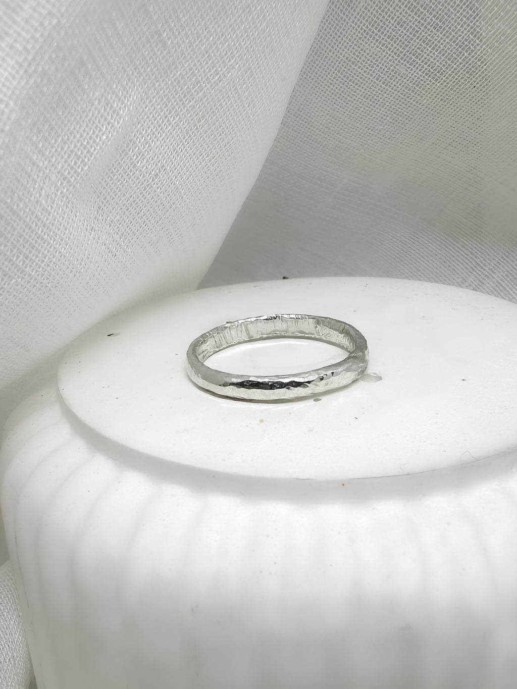Handgefertigter Silberring mit gehämmerter Oberfläche auf weißer Keramik