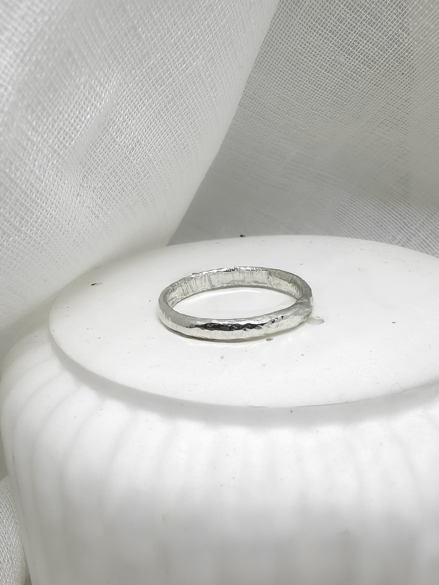 Handgefertigter Silberring mit gehämmerter Oberfläche auf weißer Keramik